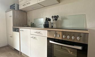 A modern kitchen with white and wood-colored cabinets. It includes a stove, a sink, and simple kitchen appliances.