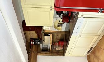 A modern kitchen with light yellow cabinets and a red refrigerator. Various kitchen appliances and dishes are arranged on the countertop.