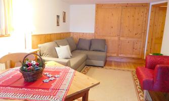 A cozy living room with a gray sofa and a red armchair. The wooden table is set with a decorative tablecloth and a flower basket.