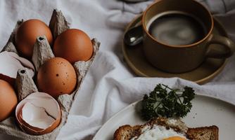 A delicious breakfast plate with a fried egg on toast. It comes with fresh eggs and a cup of coffee on a bright table.