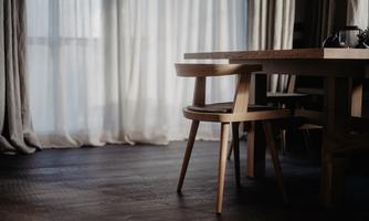 A beautiful, minimalist dining area with a wooden table and a chair. The light gently filters through the curtains, creating a warm atmosphere.