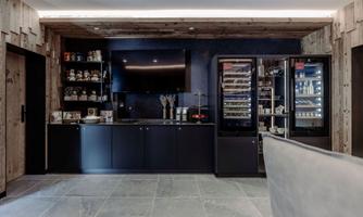A modern bar with a shelf full of drinks and snacks. The walls are made of wood and there is a large television above the counter.