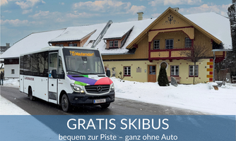 A free ski bus is driving on a snowy road. In the background, a traditional house can be seen.
