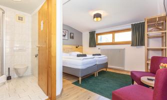 A cozy room with two single beds and a modern bathroom. The decor is bright and cheerful, with a window that lets in natural light.