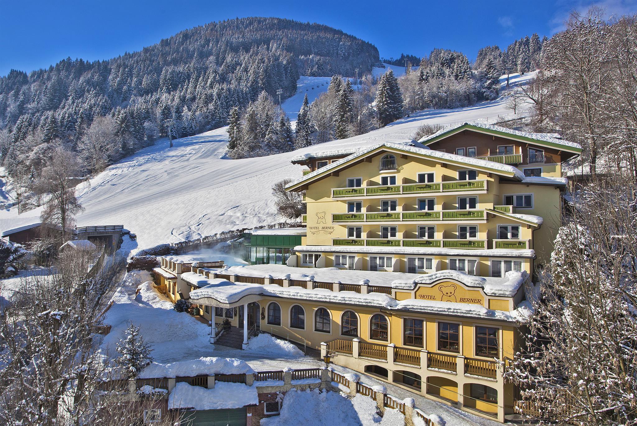 A picturesque hotel in the mountains, surrounded by snow and trees. The clear blue sky creates a relaxed winter atmosphere.