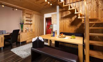 A modern room with wood paneling and a cozy staircase. There is a dining area with a table and chairs as well as a workspace in the corner.