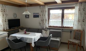 A cozy living area with a dining table, a couch, and a television. Large windows provide plenty of daylight and an inviting atmosphere.