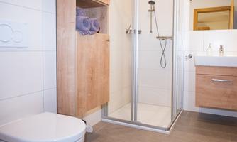 A modern bathroom with a shower, a toilet, and a sink. Wooden cabinets provide storage space and fresh towels are neatly stored.
