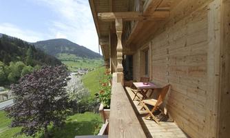 A beautiful wooden balcony with a view of green hills and mountains. On the table sits a chair and a small tabletop.