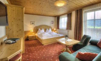 A cozy hotel room with a large bed and wooden paneling. There is a small table, a television, and a comfortable couch.