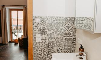 A modern bathroom with a stylish tiled wall. In the background, there is a window that suggests a cozy living atmosphere.