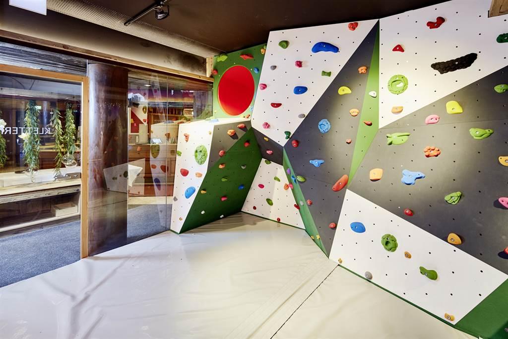 A climbing wall with colorful grips in an indoor space. The floor is covered with a soft mat.