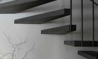 A modern staircase with floating steps made of dark wood. Below stands an elegant vase with a delicate branch.