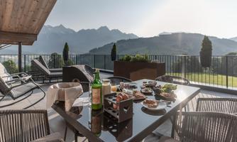 A cozy terrace with a covered table and a view of the mountains. Various dishes and drinks are served on the table.