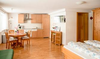 A cozy living-dining room with a kitchenette and a dining table. A bed with colorful bedding is also in the room.