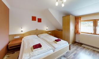 A cozy bedroom with two single beds and wooden cabinets. The large window front provides plenty of natural light and a pleasant atmosphere.
