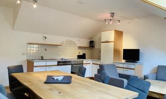A modern kitchenette with a wooden table and comfortable chairs. The room is bright and welcoming with an open layout.