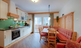 A modern kitchen with wooden details and a large dining table. Abundant light streams through the windows, creating an inviting atmosphere.