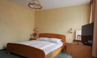 A simple bedroom with a wooden bed and a TV. The walls are painted in a light shade and there is a desk corner.