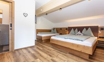 A modern bedroom with two wooden beds and a warm wooden floor. The walls are painted in light tones, providing a cozy atmosphere.