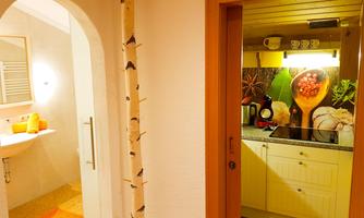 A cozy bathroom with a modern white decor and an adjacent small kitchen area. The kitchen is bright and decorated with a colorful wall design.
