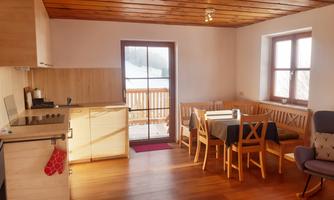 A bright, inviting apartment with a kitchenette and a dining area. Large windows offer a view of the nature outside.