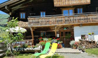 A charming wooden house with a balcony and colorful loungers in the garden. The surroundings are green with flowers and low-maintenance lawn.