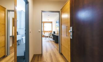A bright corridor with a wooden wardrobe and mirror and a view of a living area. The floor is wooden and the walls are in neutral colors.