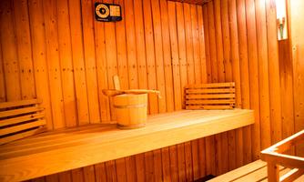 A warm sauna with wooden paneling and benches. In the center is a wooden bucket.