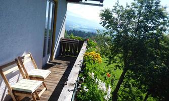 A balcony with two chairs and colorful flower boxes. In the background, green hills and a clear blue sky are visible.