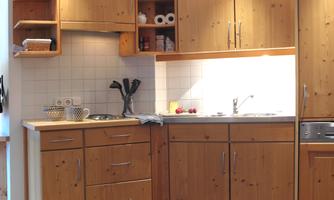 A modern kitchen made of light wood with functional cabinets. The lighting creates a pleasant atmosphere.