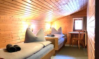 A cozy room with wooden walls and two single beds. A small table is by the window.