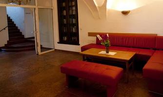 A stylish living room with red upholstered furniture and a table. In the background, a staircase can be seen leading to other rooms.