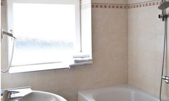 A modern bathroom with a bathtub and sink. The walls are bright, and there is plenty of daylight from a window.