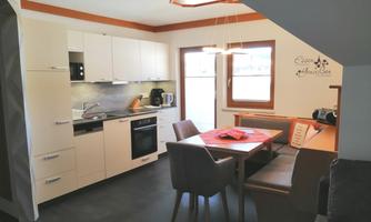 A modern kitchen with a dining table and chairs. The walls are light, and a lot of natural light comes in through the windows.