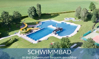 A large swimming pool with various basins and slides set amidst green spaces. The facility is surrounded by trees and is located in a quiet environment.