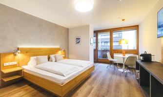 A modern studio with a double bed and a cozy dining area. Large windows provide plenty of daylight and a bright atmosphere.