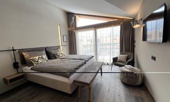 A modern bedroom with a large bed and stylish decorations. Large windows bring in plenty of daylight and offer a view outside.