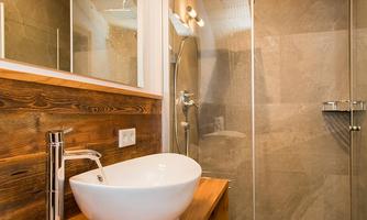 A modern bathroom with an elegant wash basin and a glass shower. The wooden elements give the space a warm atmosphere.