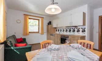 A bright and cozy kitchen with a dining area. In the background, there is a green couch and there are bright windows with curtains.