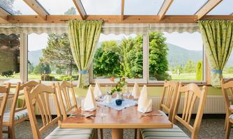 A cozy dining room with wooden furniture and table decorations. Large windows offer a view of the green landscape and the mountains.
