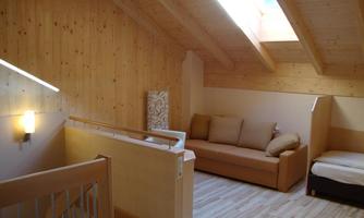 A bright, cozy room with wooden paneling and sloping ceilings. There is a seating area with a sofa and a single bed.
