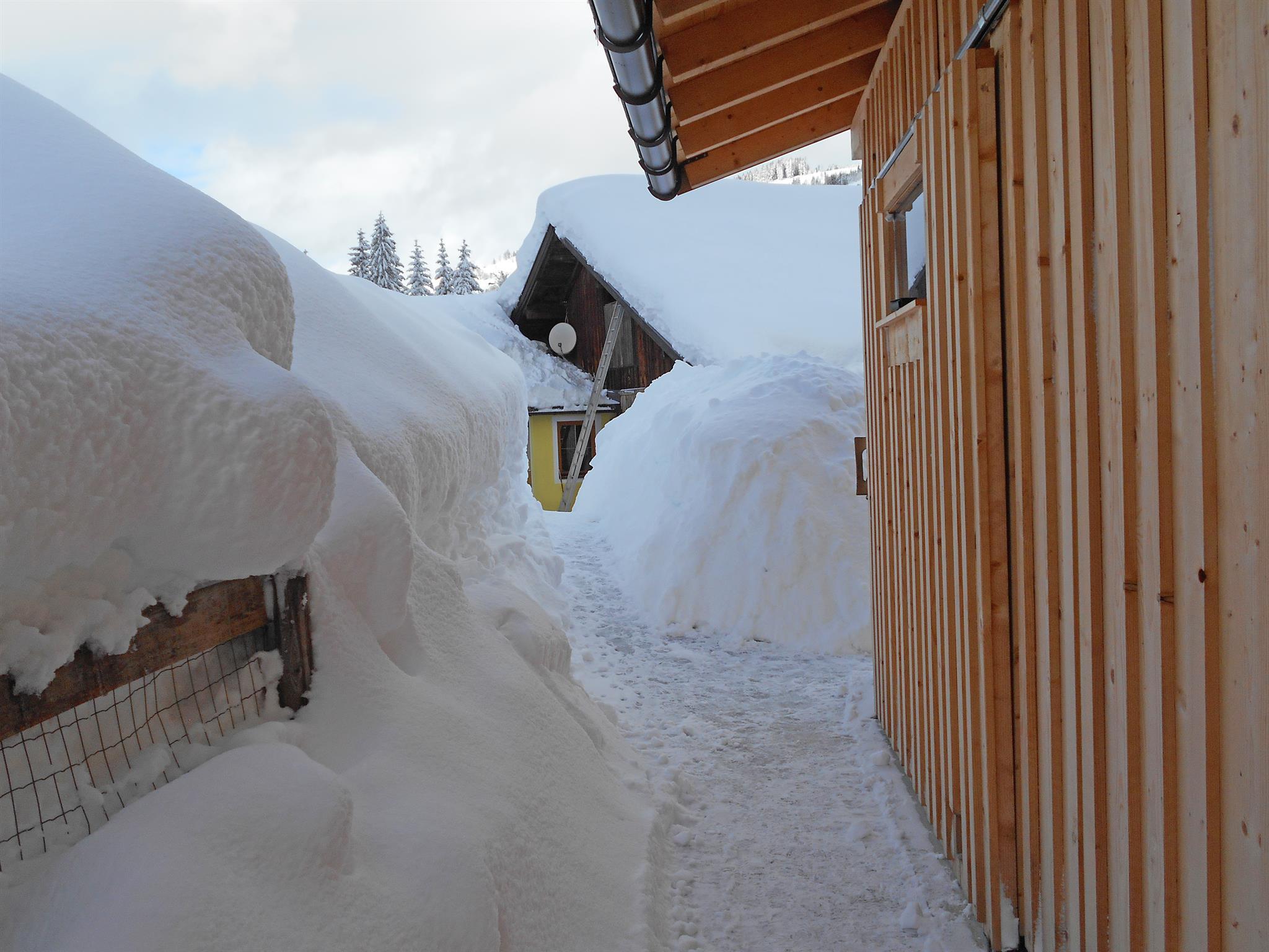 A snow-covered path between wooden houses. High snow walls surround the entrance.