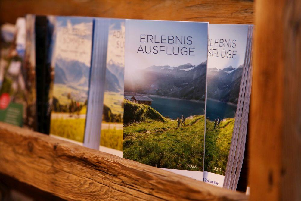A shelf with travel guides that offer excursions into nature. The brochures depict a beautiful landscape with mountains and a lake.