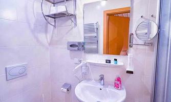A modern bathroom with shower, sink, and toilet. The walls are painted in neutral colors, and there is a mirror as well as shelves.