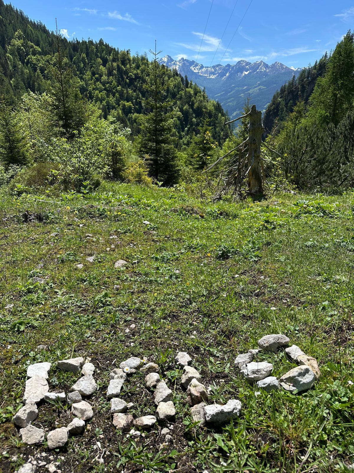 A grassland with a stone arrangement that forms "BOL". In the background, mountains and a clear blue sky can be seen.