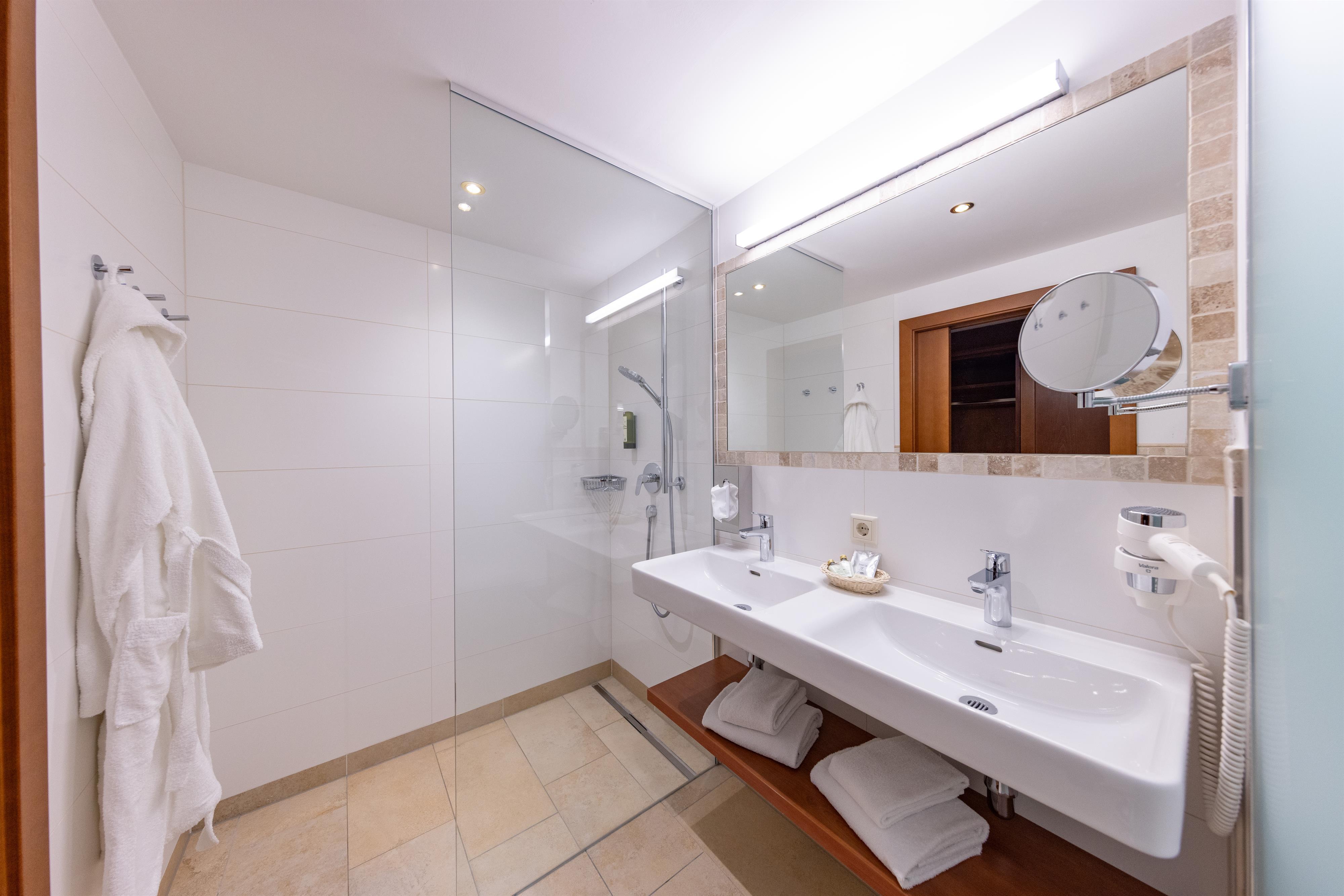 A modern bathroom with two sinks and a large mirror. There is a steam shower and fresh towels on a shelf.