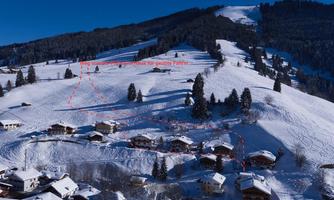 A snowy landscape with hills and small wooden houses. In the background, forests and a clear blue sky can be seen.