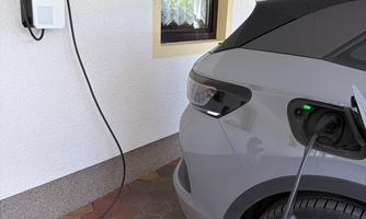 A gray electric car is charging at a charging station. The station is installed on a wall in a garage.