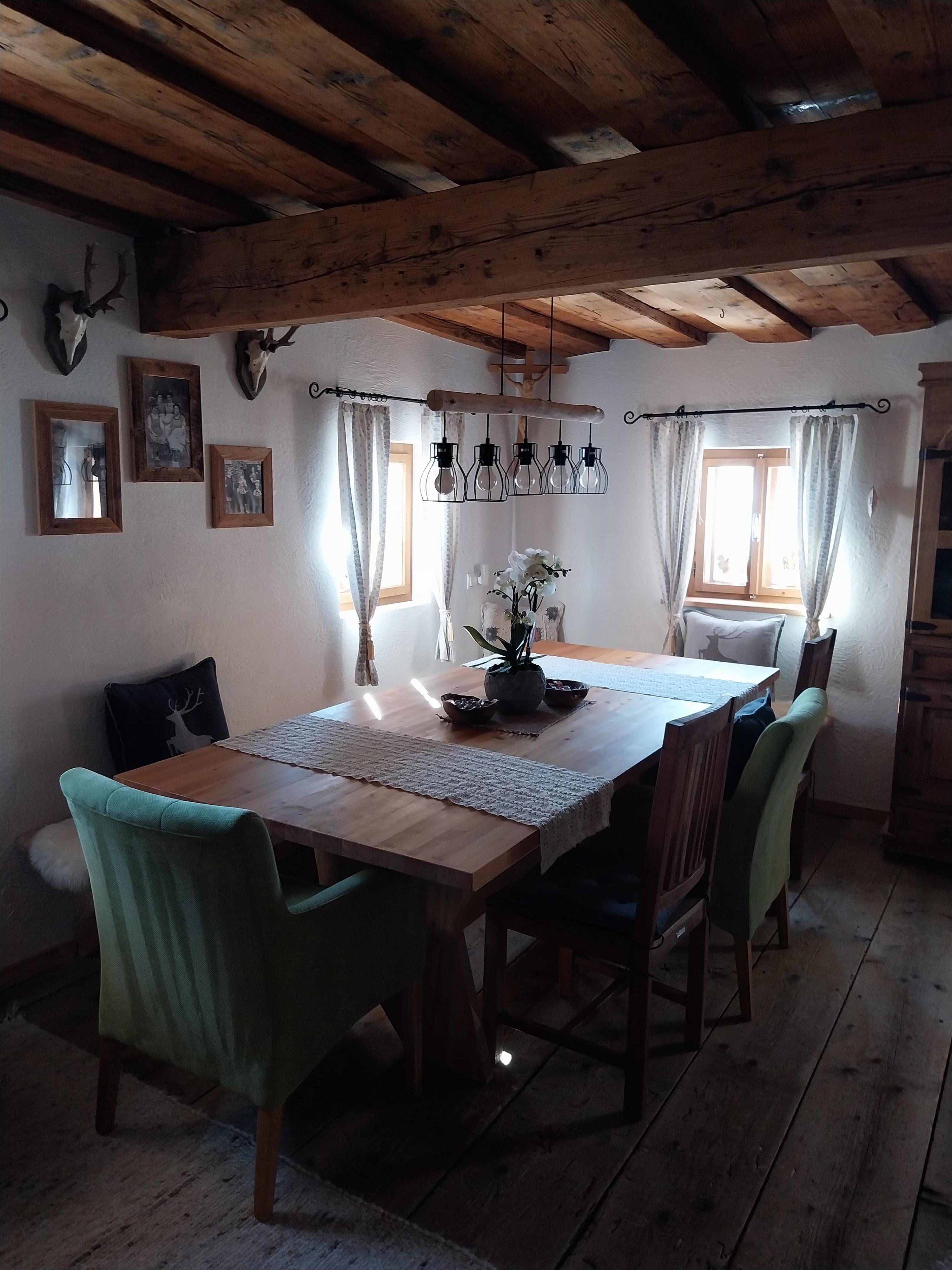 A cozy dining area with a wooden table and chairs. The walls are decorated with pictures and large windows let in plenty of light.